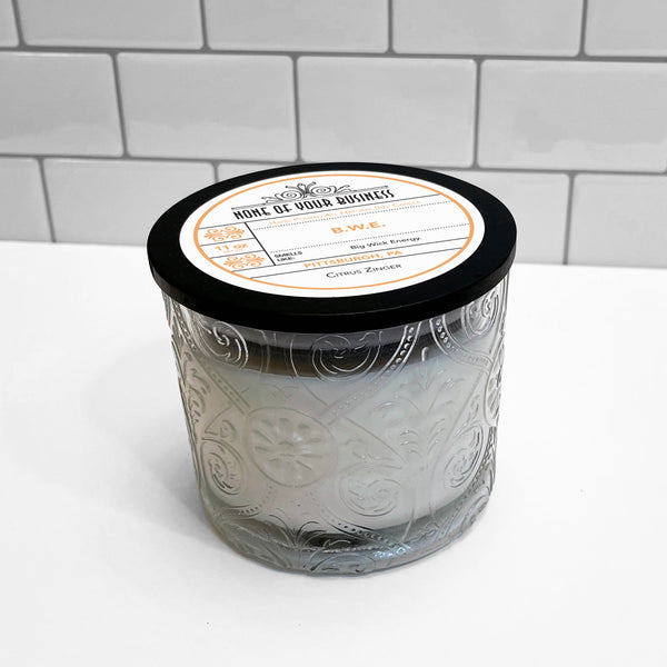 Clear Marquis glass jar with flourish pattern, white soy wax candle. Black lid with label for BWE candle.