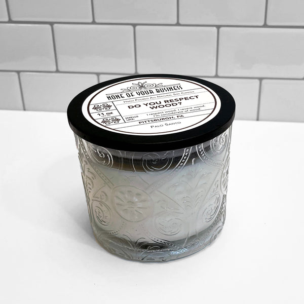 Clear Marquis glass jar with flourish pattern, white soy wax candle. Black lid with label for Do You Respect Wood candle.